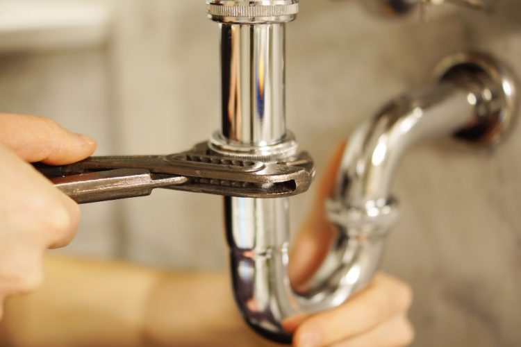 Plombier serrant un siphon chromé sous un évier avec une clé à molette